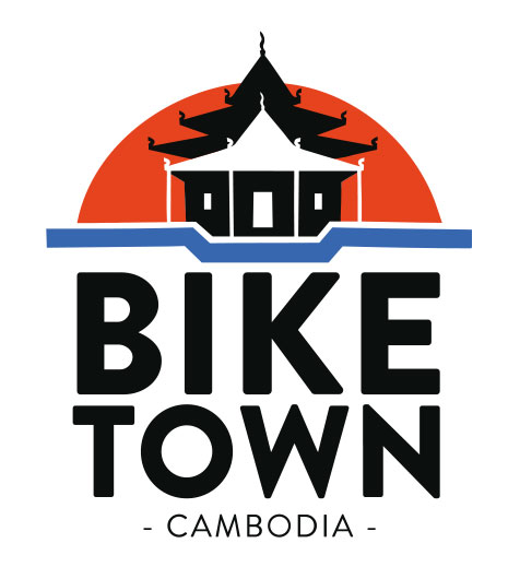 Illustrated logo featuring a Cambodian temple with a dark orange half sun rising behind it. Below the temple and sun is a blue line shaped like bicycle handlebars. The text beneath reads: 'Bike Town – Battambang Tours –'